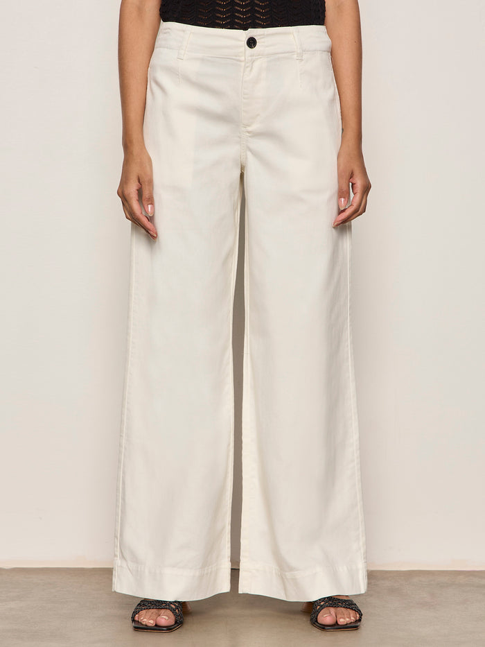 Someone wearing Sanctuary Clothing's "academy wide leg collagen" off-white trousers, a black textured top, and black open-toe sandals stands against a plain light background.