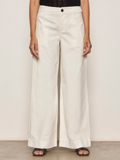 Someone wearing Sanctuary Clothing's "academy wide leg collagen" off-white trousers, a black textured top, and black open-toe sandals stands against a plain light background.