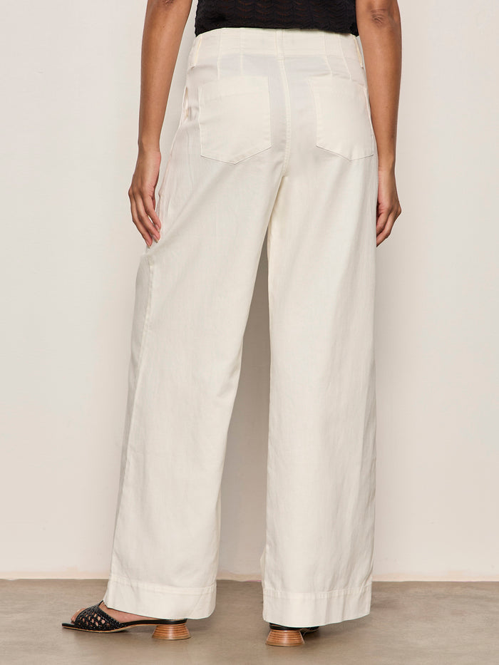 Back view of a person wearing Sanctuary Clothing’s academy wide leg collagen high-waisted, off-white pants with large back pockets, paired with black open-toed heeled sandals against a plain light background.