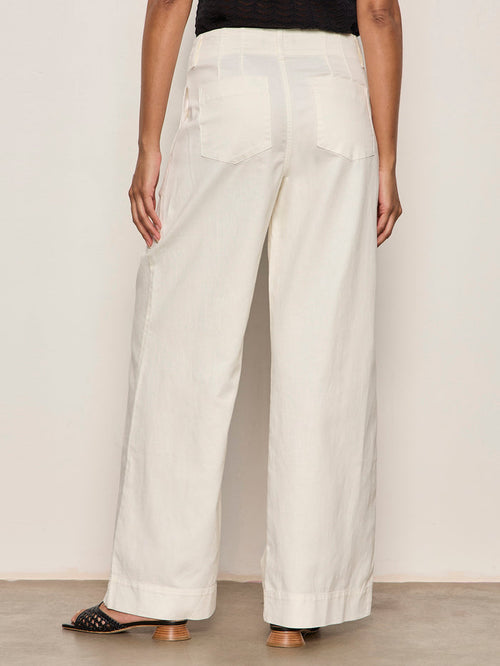 Back view of a person wearing Sanctuary Clothing’s academy wide leg collagen high-waisted, off-white pants with large back pockets, paired with black open-toed heeled sandals against a plain light background.