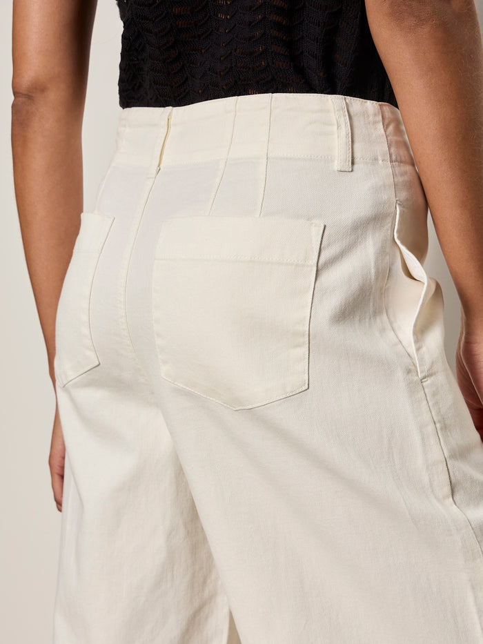 A person wears Sanctuary Clothing's academy wide leg collagen high-waisted, off-white pants with large back pockets and a black textured top; the image highlights the back of the pants from waist to mid-thigh.