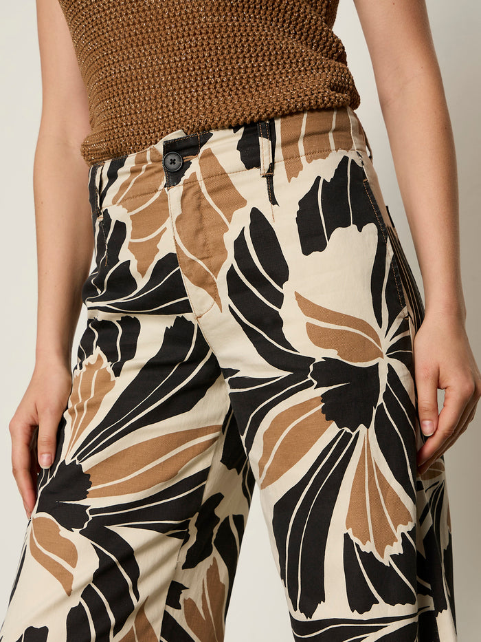 A person is wearing the Sanctuary Clothing "academy wide leg lotus" cream pants with bold black and brown floral prints, showing only their lower torso and upper legs.