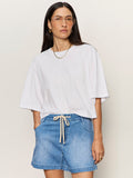 Woman with long dark hair wears clear glasses, a gold necklace, and blue drawstring denim shorts. She stands against a plain light background in the Sanctuary Clothing belle tee white.