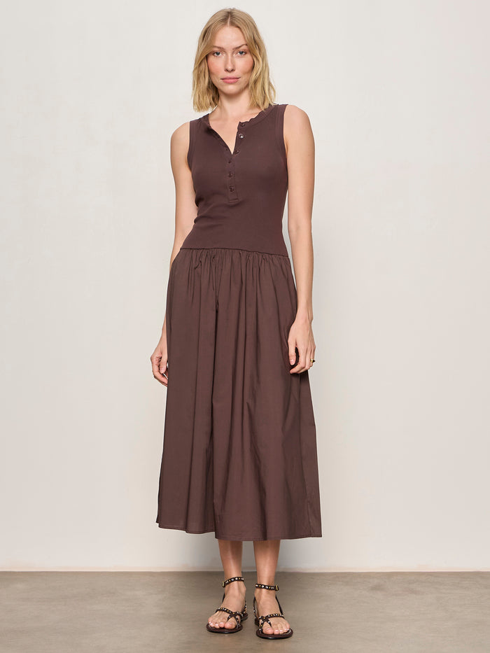 A woman with blonde hair and a relaxed expression wears the Sanctuary Clothing breakaway mix media midi dress in rich soil against a plain background, paired with black flat sandals. The dress is sleeveless, buttoned, and features a gathered skirt.