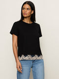 A woman wears the Sanctuary Clothing cami remix tee in black, featuring a decorative beige lace-trimmed hem, paired with light blue jeans and posed against an off-white background.