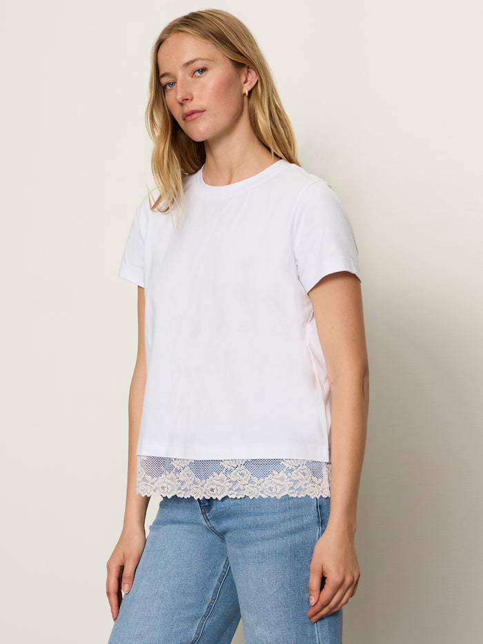 A woman with long blonde hair wears the Sanctuary Clothing cami remix tee in white and light blue jeans, standing against a plain off-white background.