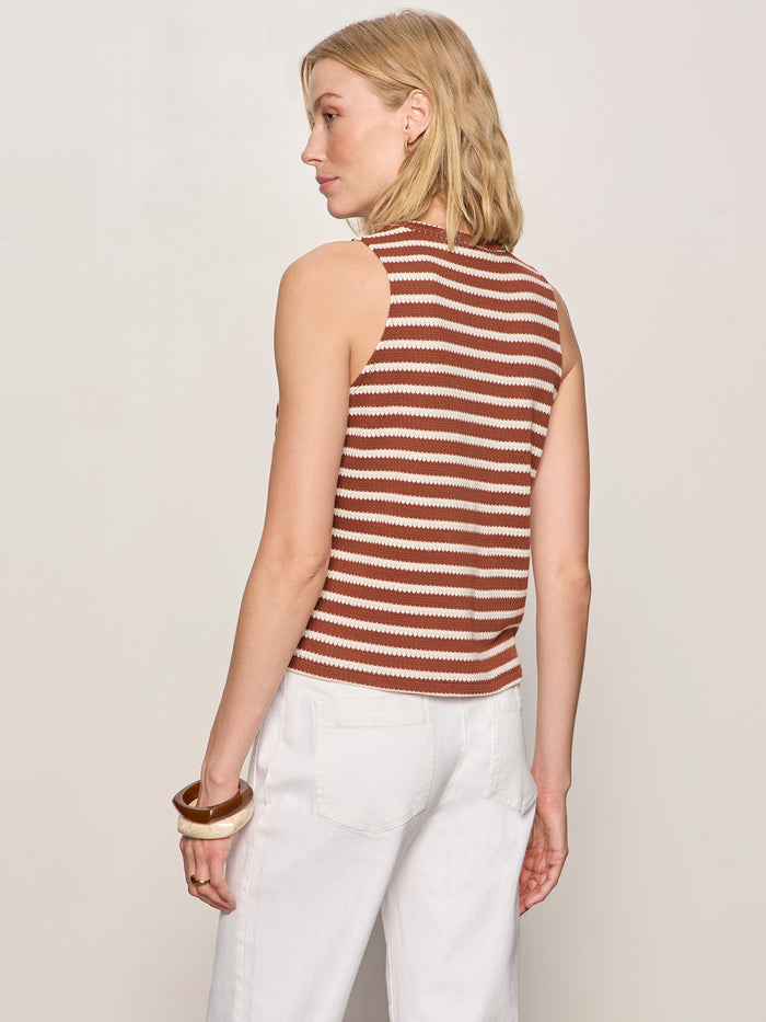 A person with shoulder-length blonde hair wears the Sanctuary Clothing campari tank in clay stripe and white pants, accessorized with bracelets on their right wrist. They stand facing away against a plain light background.