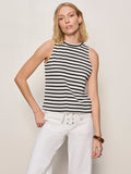 A woman with blonde hair wears the Sanctuary Clothing campari tank macrame stripe top and white lace-up pants, standing against a plain light background with a brown bangle on her wrist.
