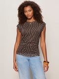 A woman with curly hair models the Sanctuary Clothing charisma dolman mesh tee rhythmic, a patterned black and brown sleeveless top, paired with light blue jeans and brown bracelets against an off-white background.