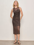 A woman with blonde hair stands against a plain light wall, wearing the Sanctuary Clothing desire more mesh cinch dress rhythmic, a sleeveless fitted black dress with a sheer white-dot overlay, paired with black sandals and her hands behind her back.