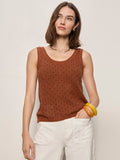 A woman with shoulder-length brown hair wears the Sanctuary Clothing dune studded tank in ancient clay and white pants, accessorized with yellow bracelets and a necklace, standing against a plain beige background.