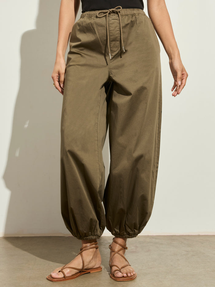 A person wears Sanctuary Clothing's "float on balloon pant timber," loose olive-green drawstring pants with elastic cuffs, paired with brown strappy sandals against a light background. Only their lower half is visible.