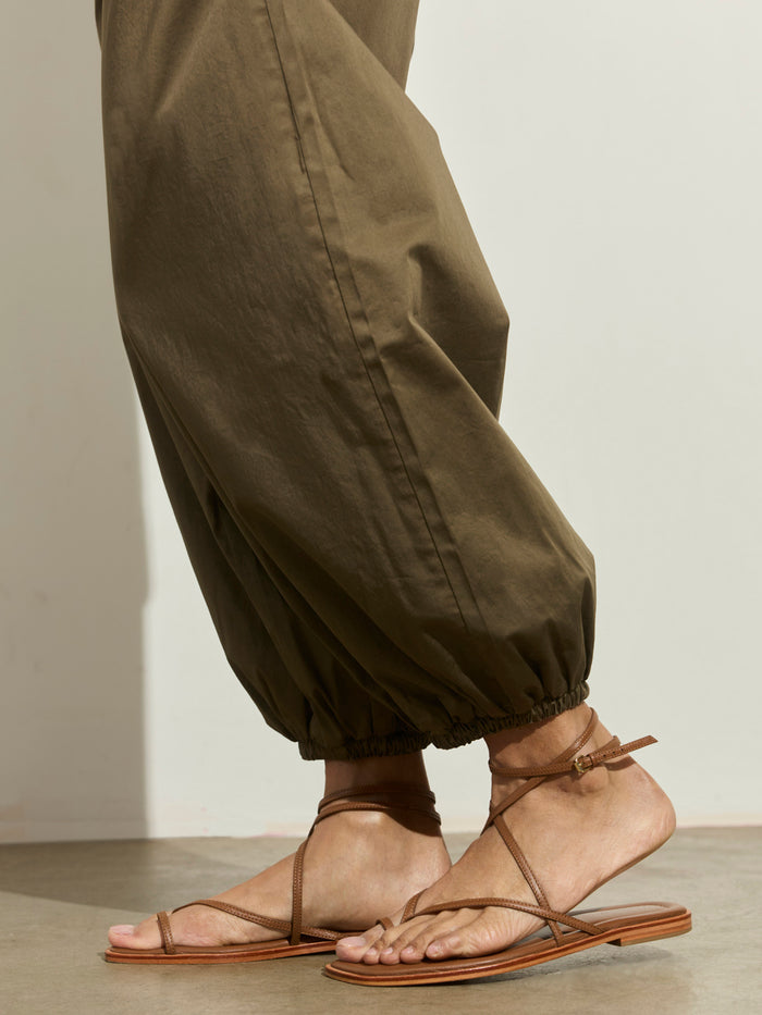 A person wearing Sanctuary Clothing's Float On Balloon Pant in Timber stands on a smooth floor, styled with brown strappy flat sandals against a plain light background.