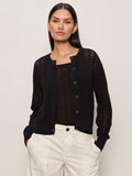 A woman with long dark hair models the Sanctuary Clothing "for keeps pointelle cardigan" in black over a matching top and light high-waisted trousers, standing with hands in pockets against a plain background.