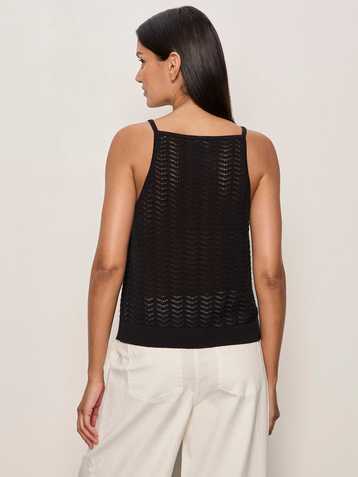 A woman with long dark hair, wearing the Sanctuary Clothing for keeps pointelle tank in black and white pants, stands facing away from the camera against a plain light background.
