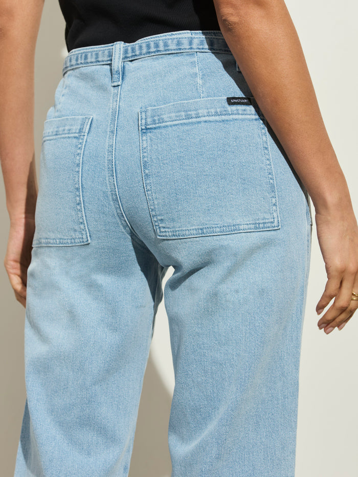 A person is shown from the waist down wearing Sanctuary Clothing's foundry jean sailor blue, featuring a high waist and large back pockets, paired with a black top against a light background.