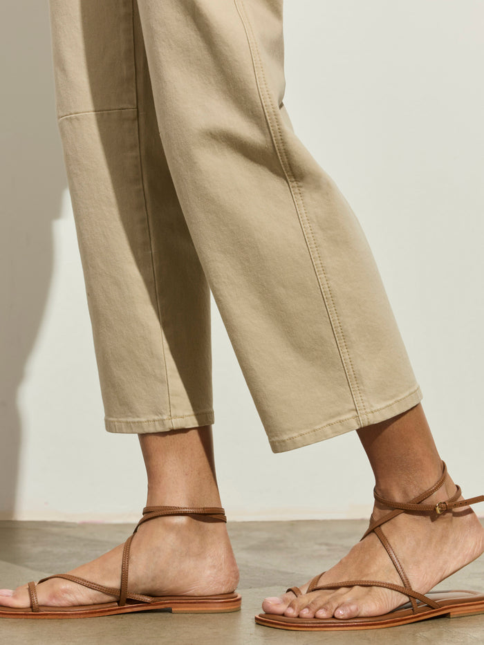 Someone wearing Sanctuary Clothing’s foundry pant khaki stands on a smooth, light floor against a neutral background, paired with brown strappy flat sandals.