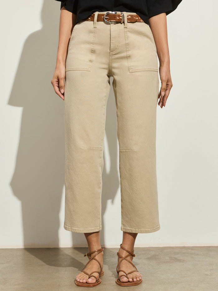 A person wearing Sanctuary Clothing's foundry pant khaki—tan, high-waisted, wide-leg pants with front patch pockets—paired with a brown belt and strappy sandals, stands against a light wall. The top half of the body is not visible.