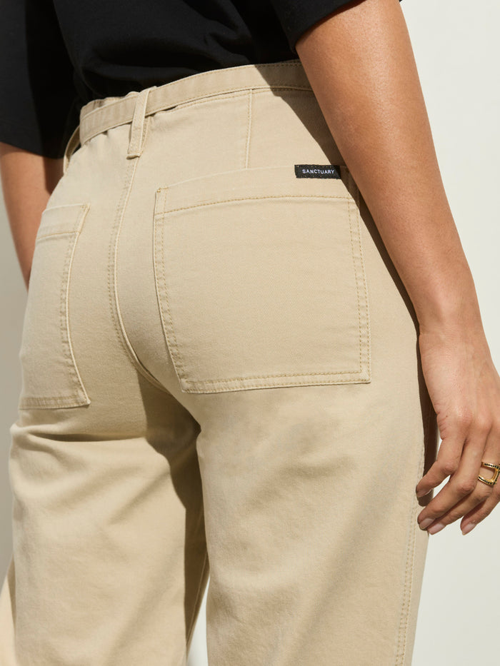 A person is shown from behind, waist down, wearing high-waisted foundry pant khaki by Sanctuary Clothing with large back pockets and a visible brand label, against a light background.