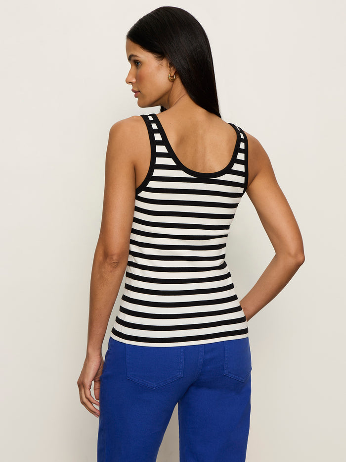 A woman with long dark hair faces away from the camera, wearing the Sanctuary Clothing go to lace up tank chalk black stripe 11 and bright blue pants against a plain light background.