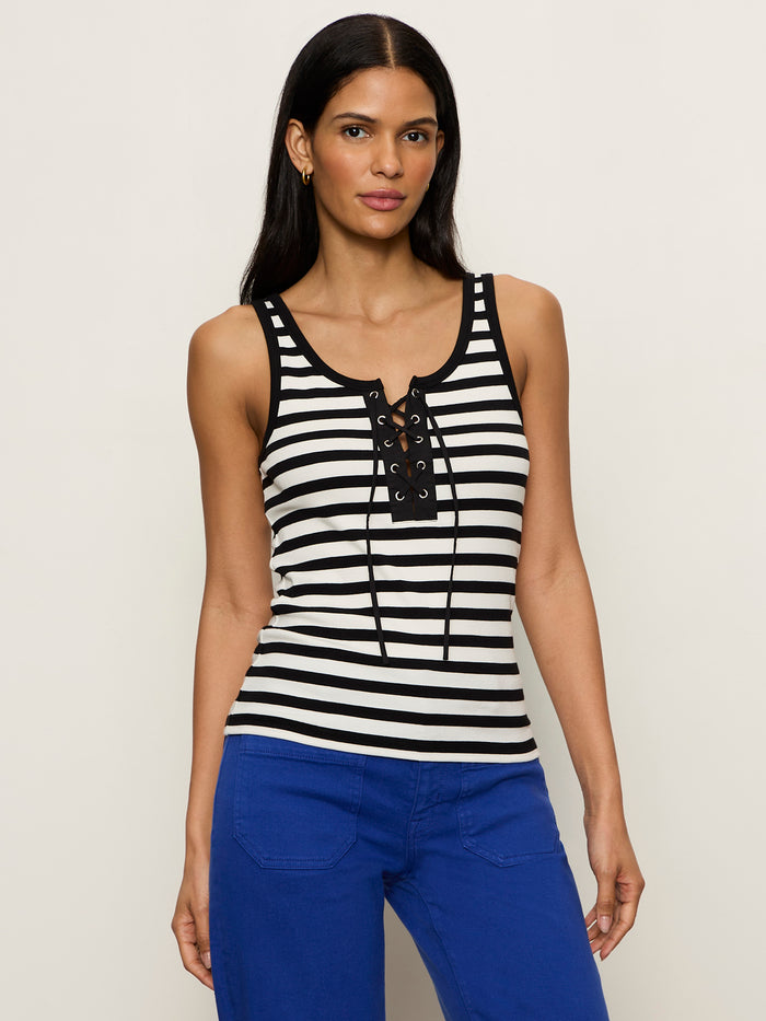 A woman wears the Sanctuary Clothing "go to lace up tank chalk black stripe 11" with blue pants, standing against a plain light background and looking at the camera with a neutral expression.
