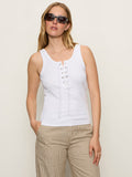 A woman wears the Sanctuary Clothing go to lace up tank in white and beige pinstriped pants, sunglasses on, standing against a plain light background with one hand in her pocket.