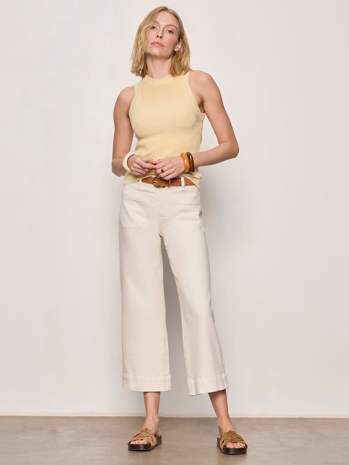 A person with blonde hair wears the Sanctuary Clothing "in the mix sweater tank banana," paired with wide-leg cream pants, a brown belt, and brown sandals. They accessorize with large bracelets and stand against a plain light background.