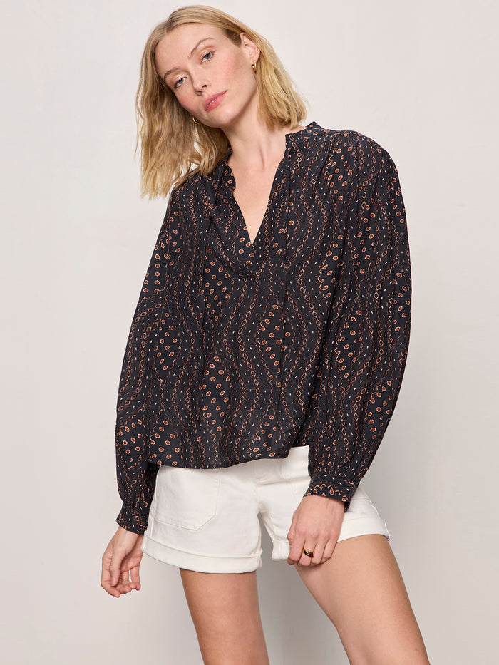A woman with shoulder-length blonde hair wears the Sanctuary Clothing joyride relaxed volume blouse rhythmic, paired with white shorts, posing against a plain light background and looking at the camera in a relaxed stance.