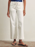 A person wearing Sanctuary Clothing's lace up mariner chalk high-waisted, wide-leg white jeans with front patch pockets, paired with black sandals, gold bangles, and a blue top stands against a neutral background.