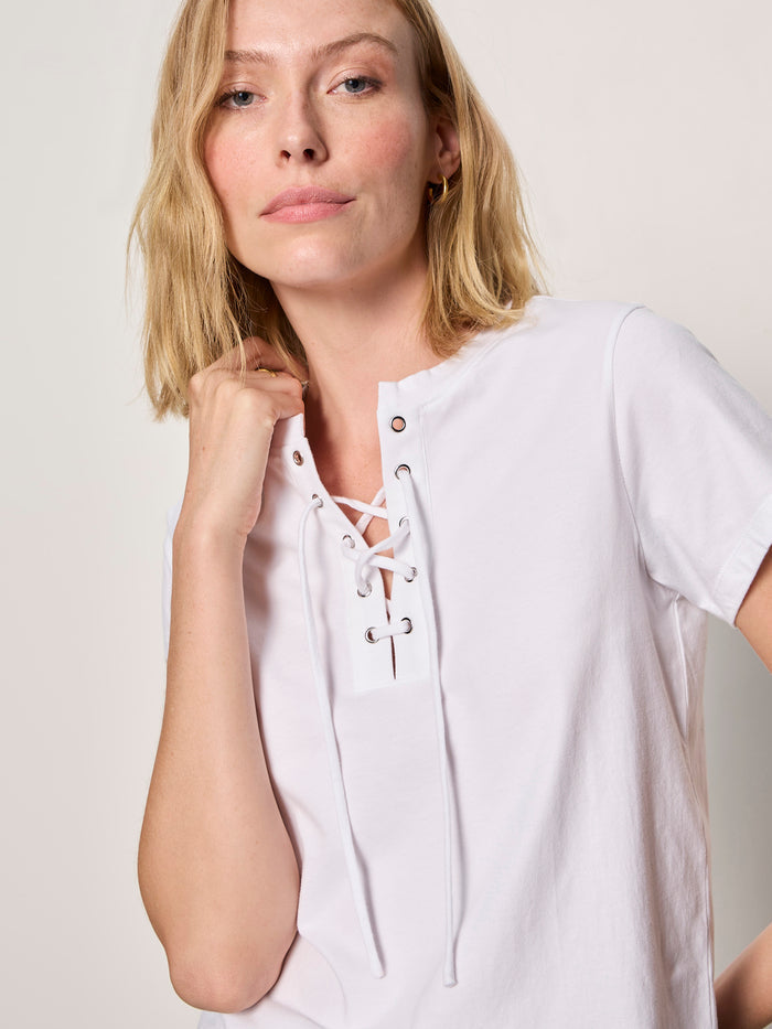 A woman with blonde hair wears the Sanctuary Clothing lace up timeless tee in white, standing against a plain light background and looking at the camera with a relaxed expression.