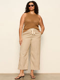 A woman with curly hair and sunglasses wears Sanctuary Clothing's lily stripe cropped pant lido stripe with a sleeveless brown knit top and black heels, posing against a plain background with her hand in her pocket.