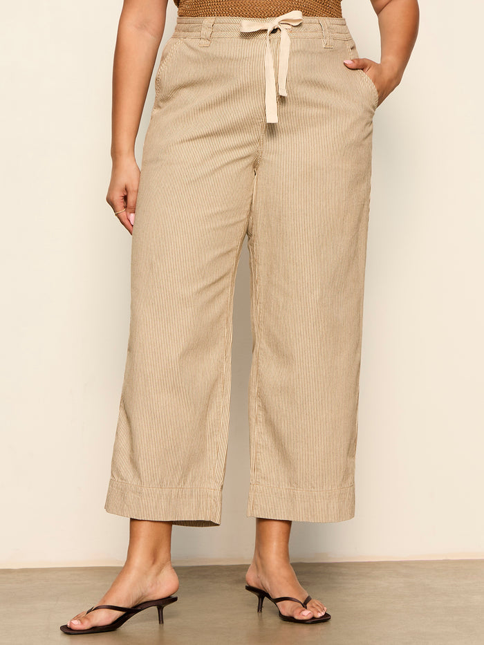 A person wears Sanctuary Clothing's lily stripe cropped pant lido stripe (extended sizing), featuring a beige, wide-leg, ankle-length silhouette with a drawstring waist and hands in pockets, paired with black open-toe heeled sandals.