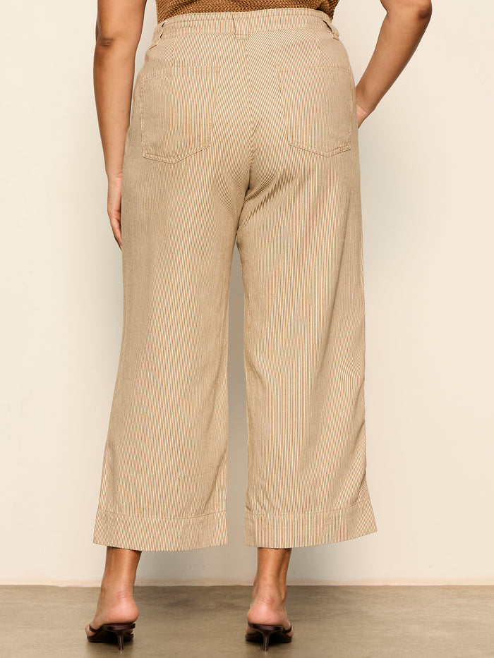 A person faces away from the camera, modeling Sanctuary Clothing's lily stripe cropped pant in lido stripe, shown from waist to ankles. The high-waisted, wide-leg pants feature back pockets and are paired with brown heeled sandals. Extended sizing available.