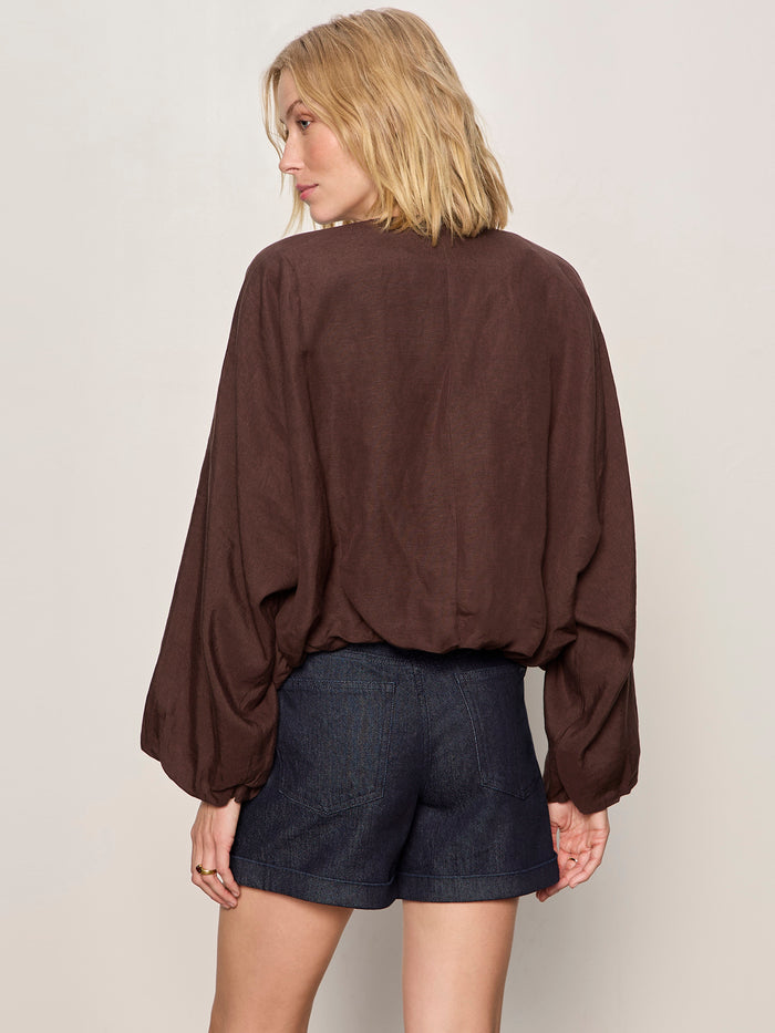 A woman with shoulder-length blonde hair is seen from behind, wearing the Sanctuary Clothing linen bubble jacket in rich soil against a plain light background.