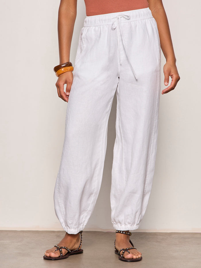 A person wearing the "melody micro linen balloon white" jogger pants by Sanctuary Clothing, styled with flat studded sandals and chunky bracelets, stands against a plain light background.