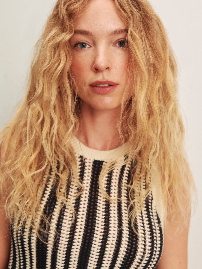 A woman with long, wavy blonde hair and blue eyes wears the Sanctuary Clothing natural state halter tank cabana stripe. She stands against a plain, light background and looks at the camera.