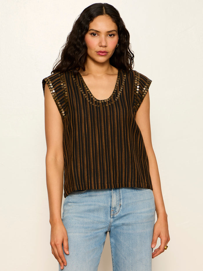 A woman with long wavy dark hair wears the Sanctuary Clothing "outsider embellished shell top" in dark cumin black stripe, styled with light blue jeans, standing against a plain light background.