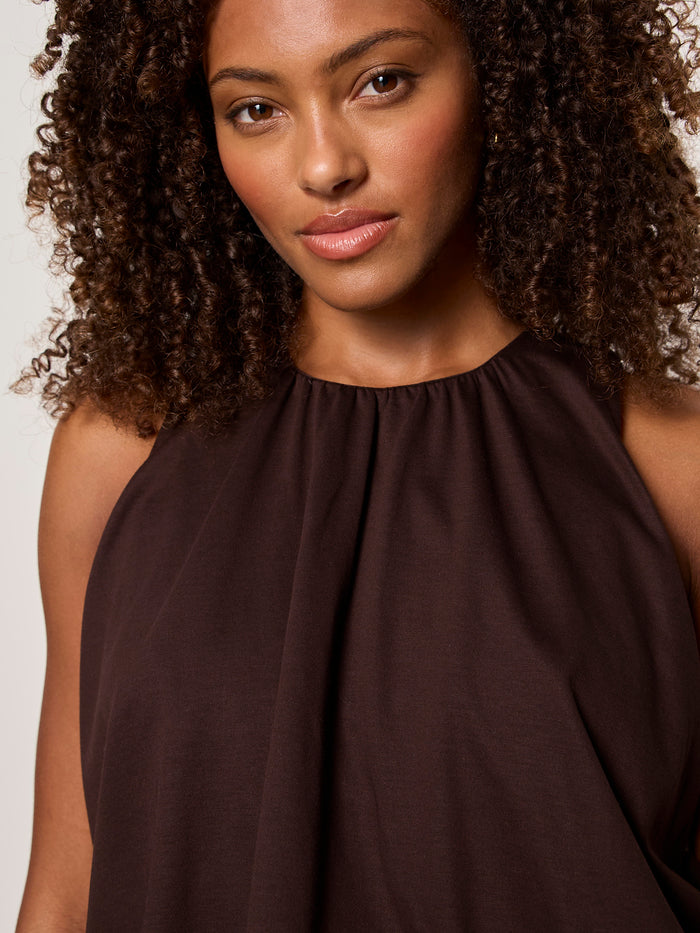 A woman with curly brown hair wears the Sanctuary Clothing retreat bubble tank in rich soil and gazes softly at the camera against a plain background.