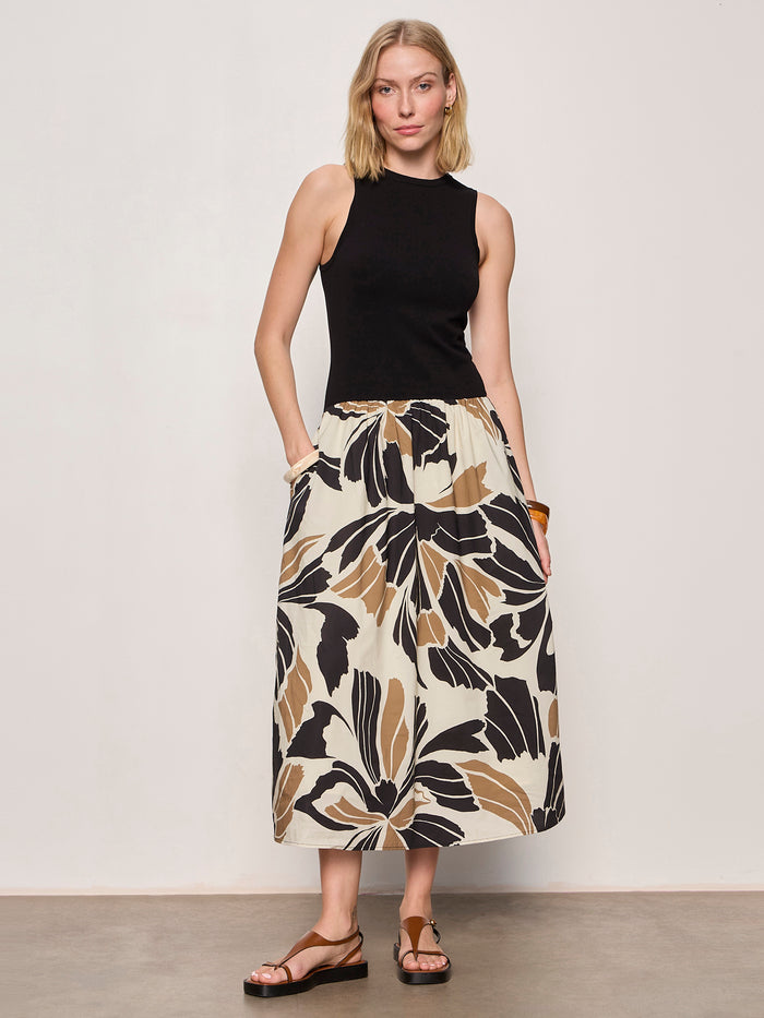 A woman stands against a plain background wearing Sanctuary Clothing's sandbar mix media midi dress in lotus w black, paired with brown sandals and a bracelet, with her hands in the dress pockets.