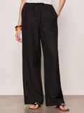 A person stands against a plain light background wearing Sanctuary Clothing shoreline linen pants in black, paired with a white sleeveless top, black flat sandals, and a brown bangle on their left wrist.