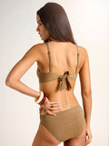 Woman with long dark hair, shown from the back, wears the Sanctuary Clothing side shirred hipster bikini bottom in toasted coconut. She has one hand on her hip and accessorizes with bracelets and rings against a neutral background.