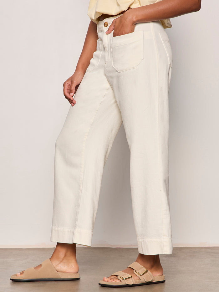A person wearing Sanctuary Clothing's Soft Marine Wide Leg Crop Pant Collagen in off-white, paired with a beige short-sleeve top and tan slide sandals with buckles, stands against a plain background.