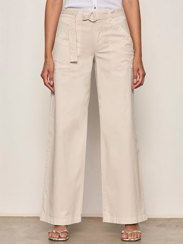 A person wears Sanctuary Clothing's Soft Polished Wide Leg Summer Sand trousers with a matching belt, paired with a white sleeveless top and open-toe sandals, standing against a neutral background.