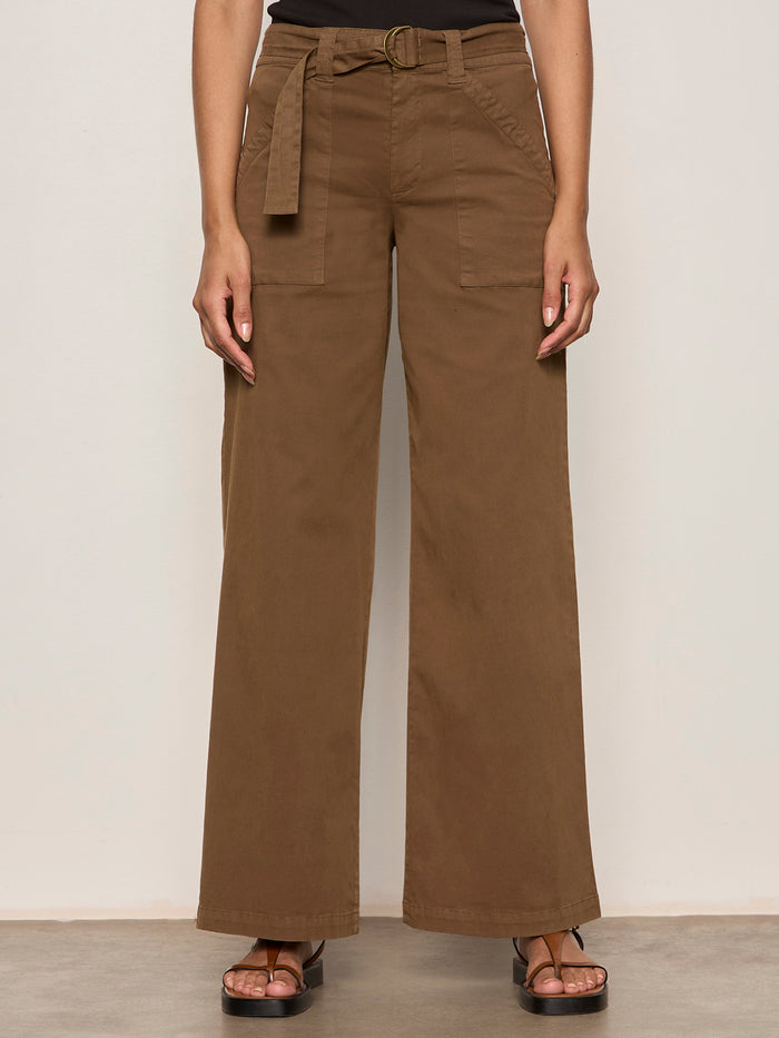 Someone stands against a light background, wearing Sanctuary Clothing’s "soft polished wide leg timber" high-waisted brown pants with a matching belt, paired with a black top and brown sandals. Only the body from shoulders down is visible.