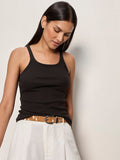 A woman with long dark hair wears the Sanctuary Clothing sprinter rib tank in black, paired with white high-waisted pants and a brown belt. She looks down with a slight smile against a plain light background.