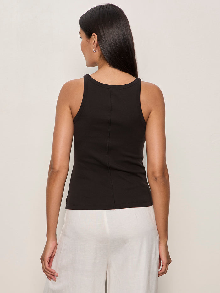A woman with long dark hair, seen from the back, wears the Sanctuary Clothing sprinter rib tank in black and loose white pants against a plain light background.