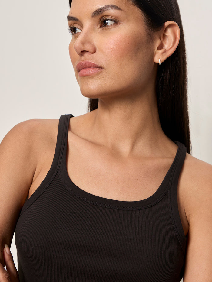 A woman with long dark hair and light skin wears the Sanctuary Clothing sprinter rib tank in black and a small hoop earring, gazing to the side with a neutral expression against a plain background.
