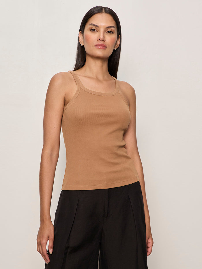 A woman with long dark hair wears Sanctuary Clothing's sprinter rib tank in toasted coconut and loose black pants, standing against a plain light background facing forward with a neutral expression.