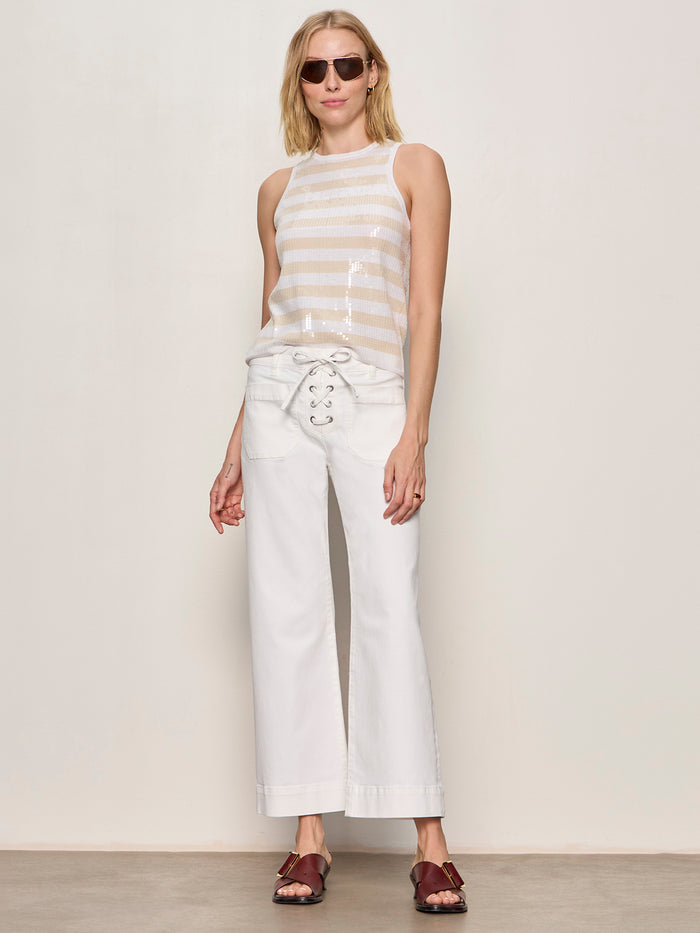 A woman in Sanctuary Clothing's summer shine sequin shell summer sand white stripe top pairs it with high-waisted white wide-leg pants and brown sandals, standing against a light wall.