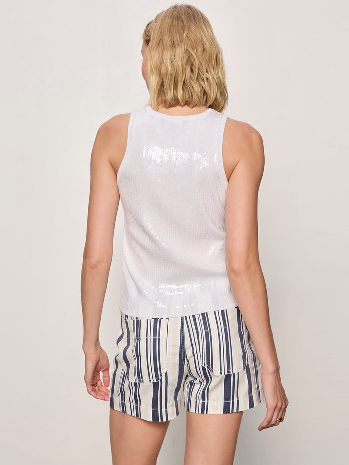 A person with short blonde hair is seen from the back, wearing Sanctuary Clothing's "summer shine sequin shell white" top and striped shorts with blue, black, and beige vertical lines against a plain light background.